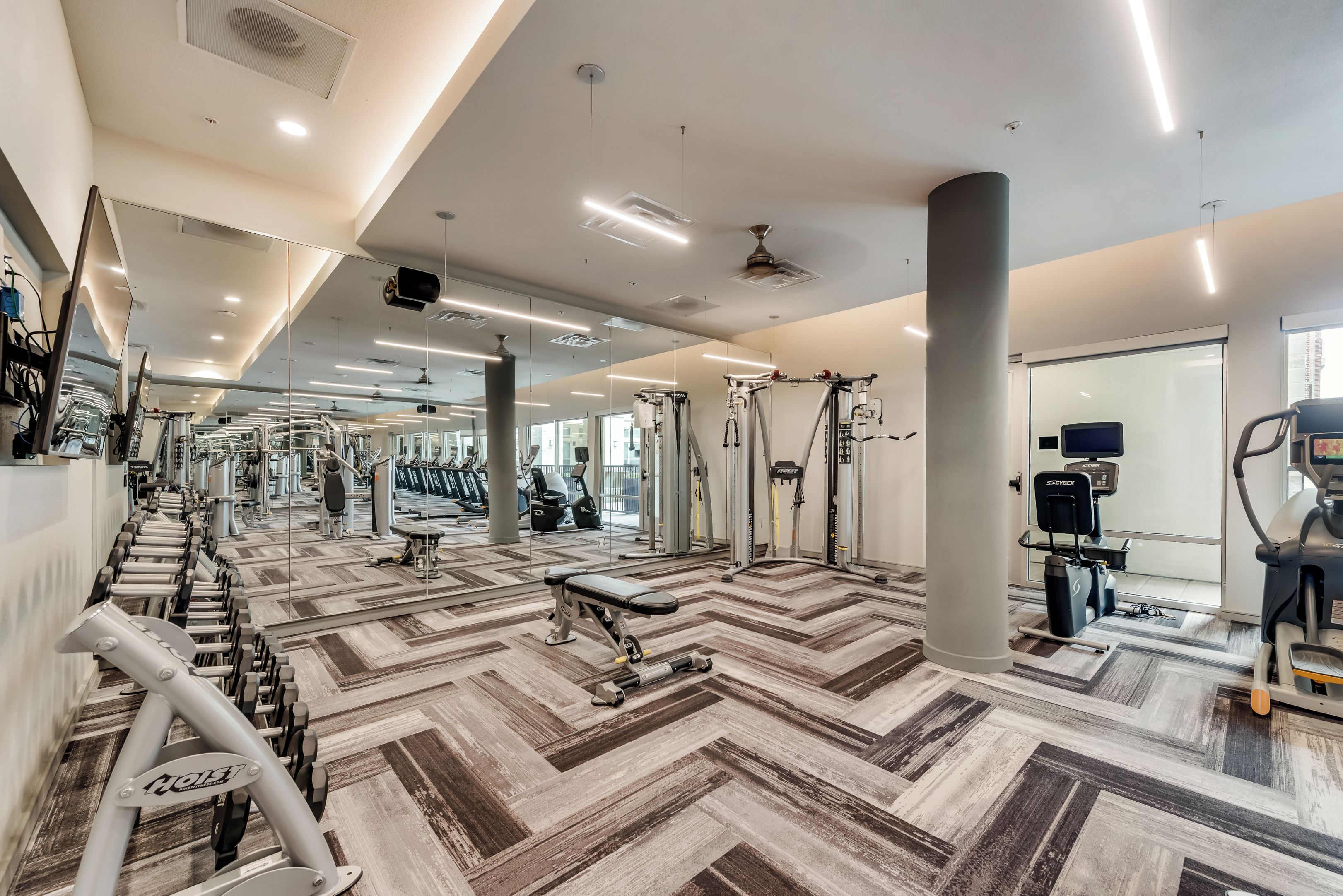 Un gimnasio con equipos de ejercicio variados, paredes espejadas y un suelo estampado.