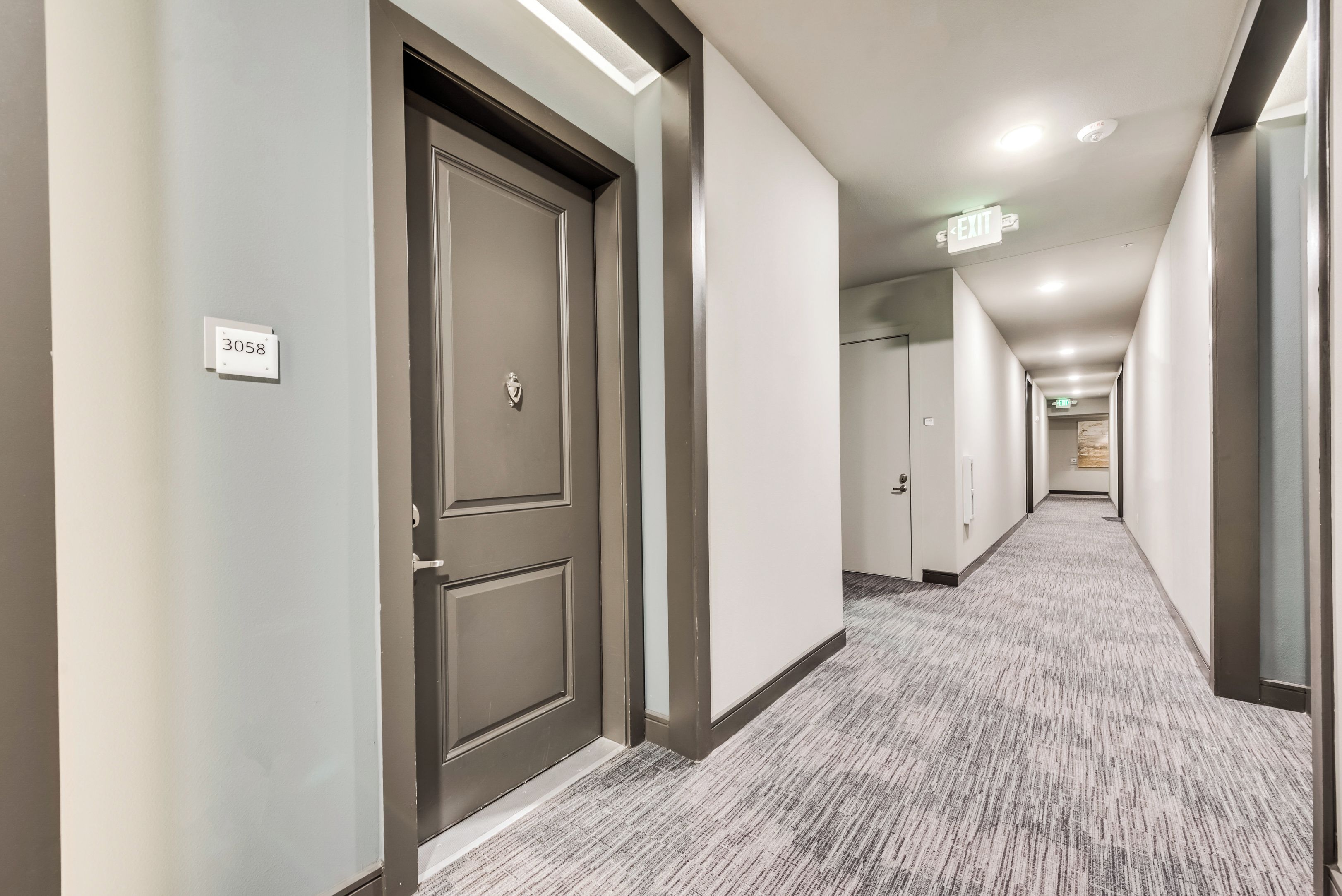 Passadís d'hotel amb portes, sòl amb moqueta i un senyal de sortida.