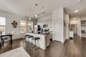 A modern kitchen with white cabinets, a central island with bar stools, and a dining area with a table and chairs.