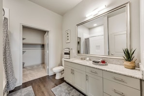 Un baño moderno con inodoro, lavamanos y espejo. Cuenta con una zona de ducha con cortina y una planta en el mostrador.