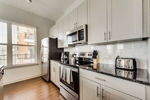 A modern kitchen with stainless steel appliances, white cabinetry, and a window with blinds.