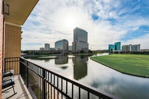 A river with a bridge, a grassy area, and several buildings in the background.