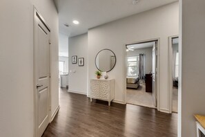 A hallway with a white door, a white console table with a mirror, and a view into a bedroom with a bed and a window. - LC058-3 - Home|Yard|8mi to Fair Park|Sleeps 6 (Irving)