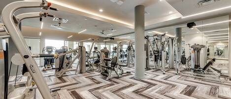 A gym with various exercise equipment, a patterned floor, and a ceiling with recessed lighting.