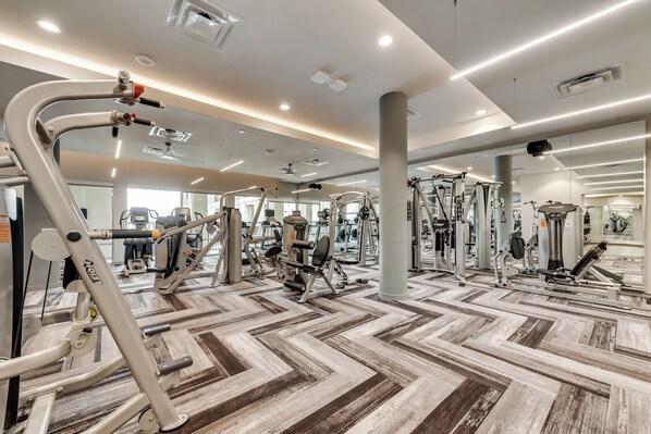 A gym with various exercise equipment, a patterned floor, and a ceiling with recessed lighting.