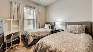 A hotel room with two beds, a desk, a chair, a nightstand, and a ceiling fan.