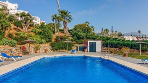 Una piscina con sillas de descanso, rodeada de follaje y un muro de piedra.