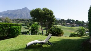 Una silla de descanso en un césped cuidado, con un campo de golf y montañas al fondo.