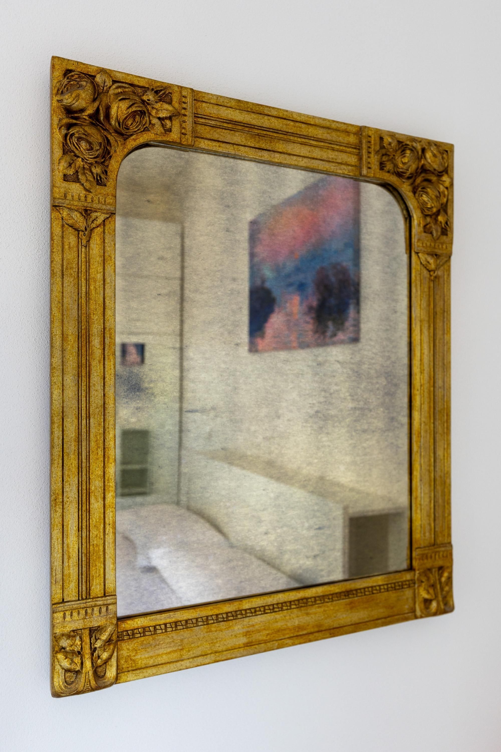Un miroir doté d’un cadre doré orné, qui reflète une pièce comprenant un lit et un tableau accroché au mur.