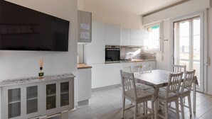 A modern kitchen with white cabinets, a built-in oven, and a dining area with a table and chairs.