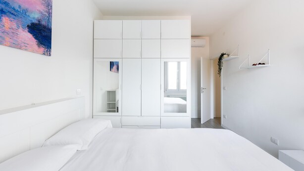 A modern bedroom with a large bed, a wardrobe, and a painting on the wall.