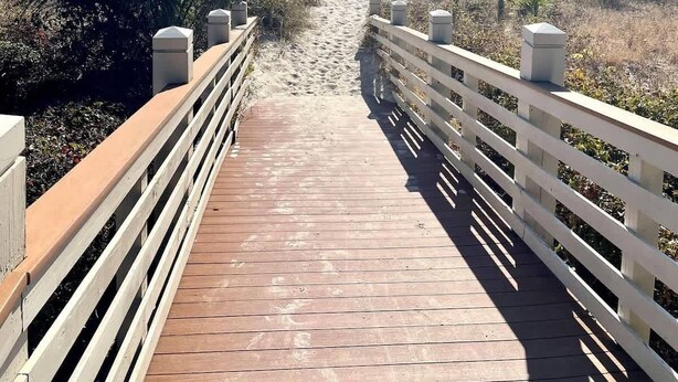 A wooden boardwalk leading to a beach with a sign indicating a nature reserve.