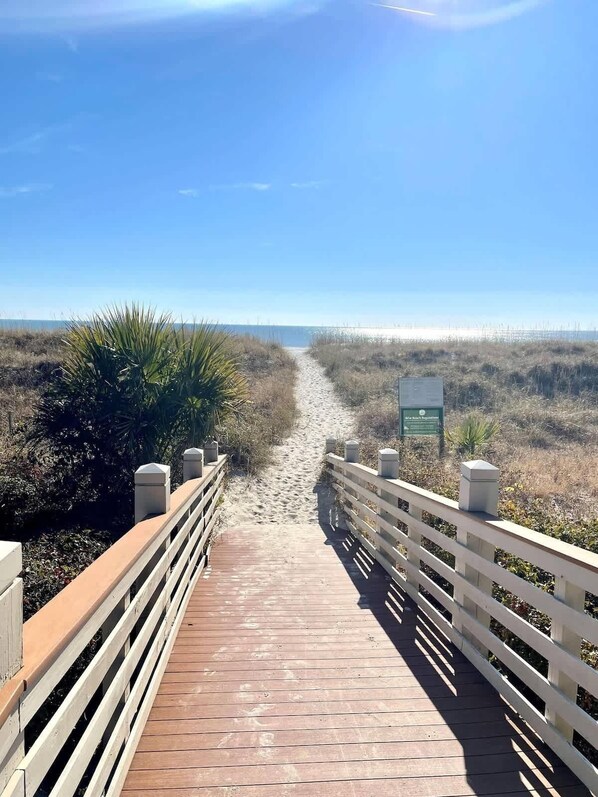 A wooden boardwalk leading to a beach with a sign indicating a nature reserve.