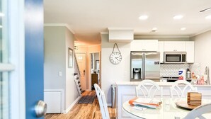 A modern kitchen with white cabinets, a stainless steel refrigerator, a microwave, and a clock on the wall.