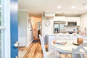 A modern kitchen with white cabinets, a stainless steel refrigerator, a microwave, and a clock on the wall.