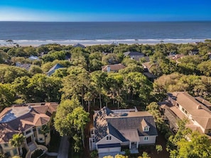 An aerial view of a coastal residential area with houses, trees, and a beach.