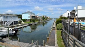 A canal with houses on either side, a wooden dock, and a small bush. - Oceanfront Queen's Grant Condo "Tide-the-Knot" with Breathtaking Ocean Views! (Topsail Beach)
