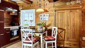 A wooden interior with a kitchen area featuring a table with chairs, a hanging light fixture, and a wooden cabinet. - Rustikales Studio-apartment Blockstube im FH Selma (Großschönau)