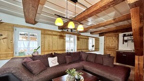 A cozy living room with a large sectional sofa, wooden beams, and a ceiling light fixture. - Rustikales Studio-apartment Blockstube im FH Selma (Großschönau)