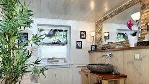 A bathroom with a wooden vanity, a stone sink, a large mirror, and a window with blinds. - Rustikales Studio-apartment Blockstube im FH Selma (Großschönau)