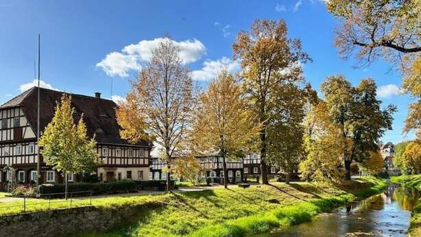 A traditional half-timbered building with a river in front. - Rustikales Studio-apartment Blockstube im FH Selma (Großschönau)