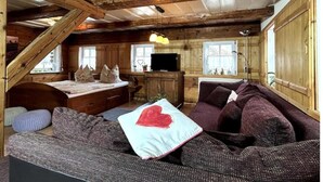 A cozy cabin interior with a loft bed, a sofa, and a television. - Rustikales Studio-apartment Blockstube im FH Selma (Großschönau)