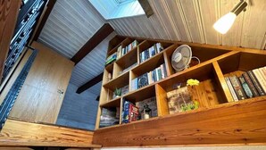 Un coin lecture confortable, avec des étagères en bois remplies de livres, un petit ventilateur et des objets décoratifs.