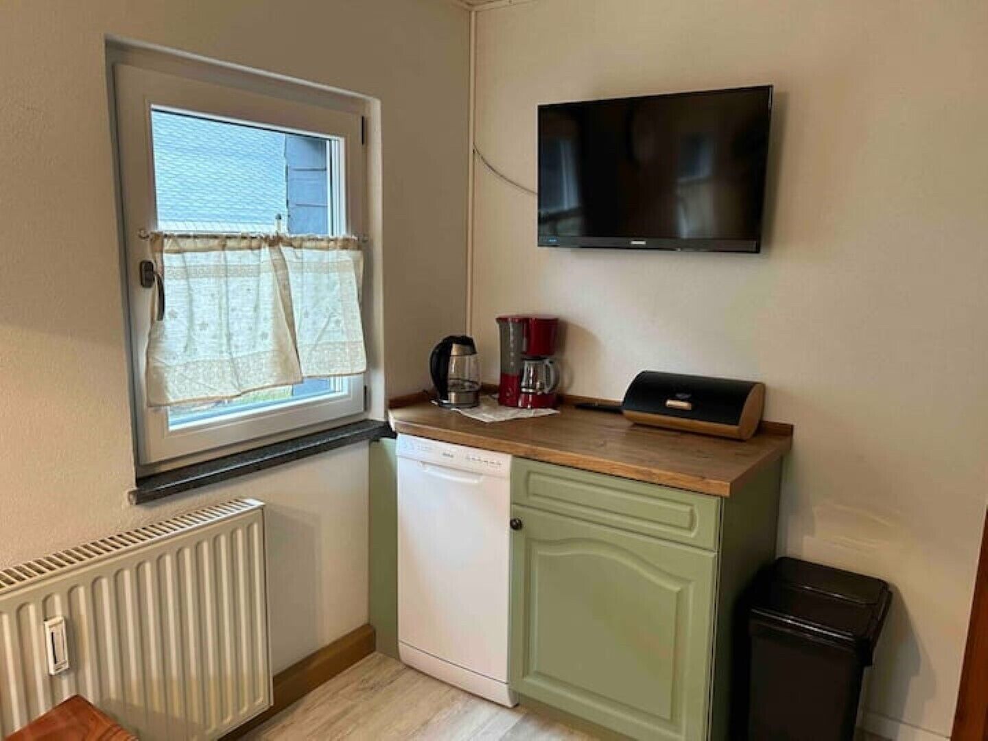 Una cocina compacta con ventana, televisor de pared, cafetera y un cubo de basura.