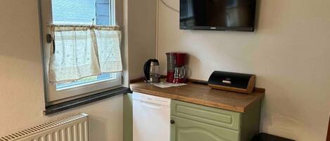 Una cocina compacta con ventana, televisor de pared, cafetera y un cubo de basura.