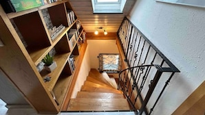 Un escalier en bois, surmonté d’une lucarne, mène à un palier agrémenté d’une rampe en métal décorative.