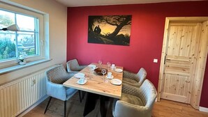 A dining area with a table set for four, a window with a view, and a red wall with a painting.