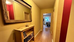 A hallway with wooden flooring, a wooden console table with books, a mirror, and a red wall.