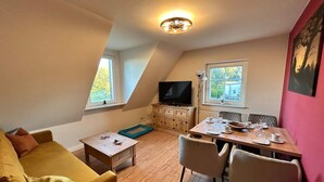 A cozy loft apartment with a dining area, a TV, and a large window providing natural light.