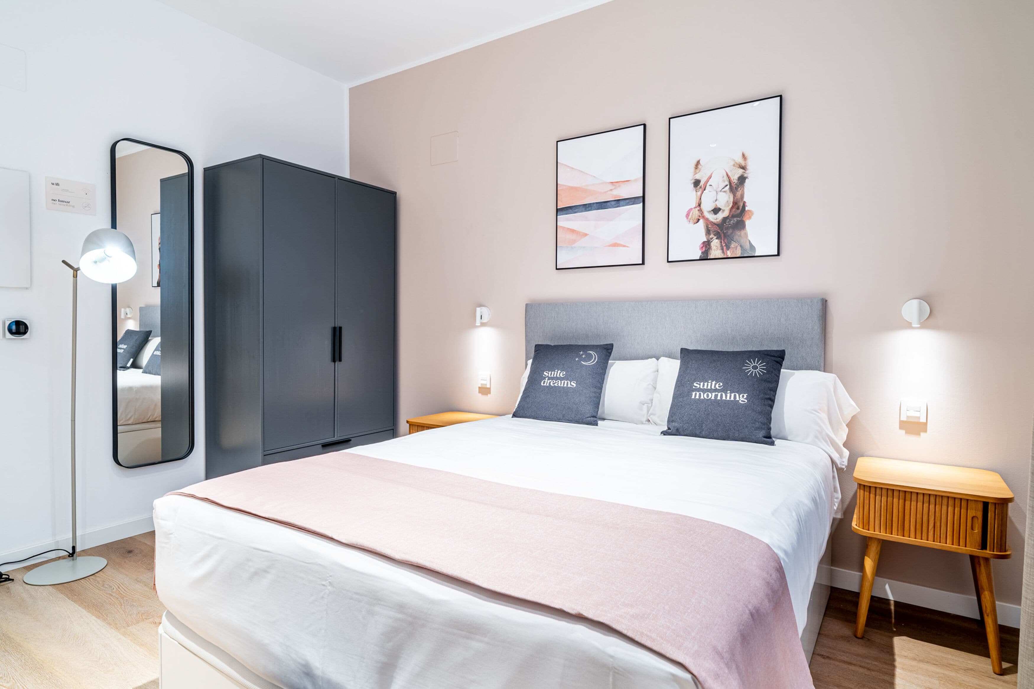 Quarto de hotel moderno com cama grande, guarda-roupa, mesas de cabeceira e obras de arte penduradas na parede.