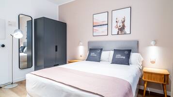 Quarto de hotel moderno com cama grande, guarda-roupa, mesas de cabeceira e obras de arte penduradas na parede.