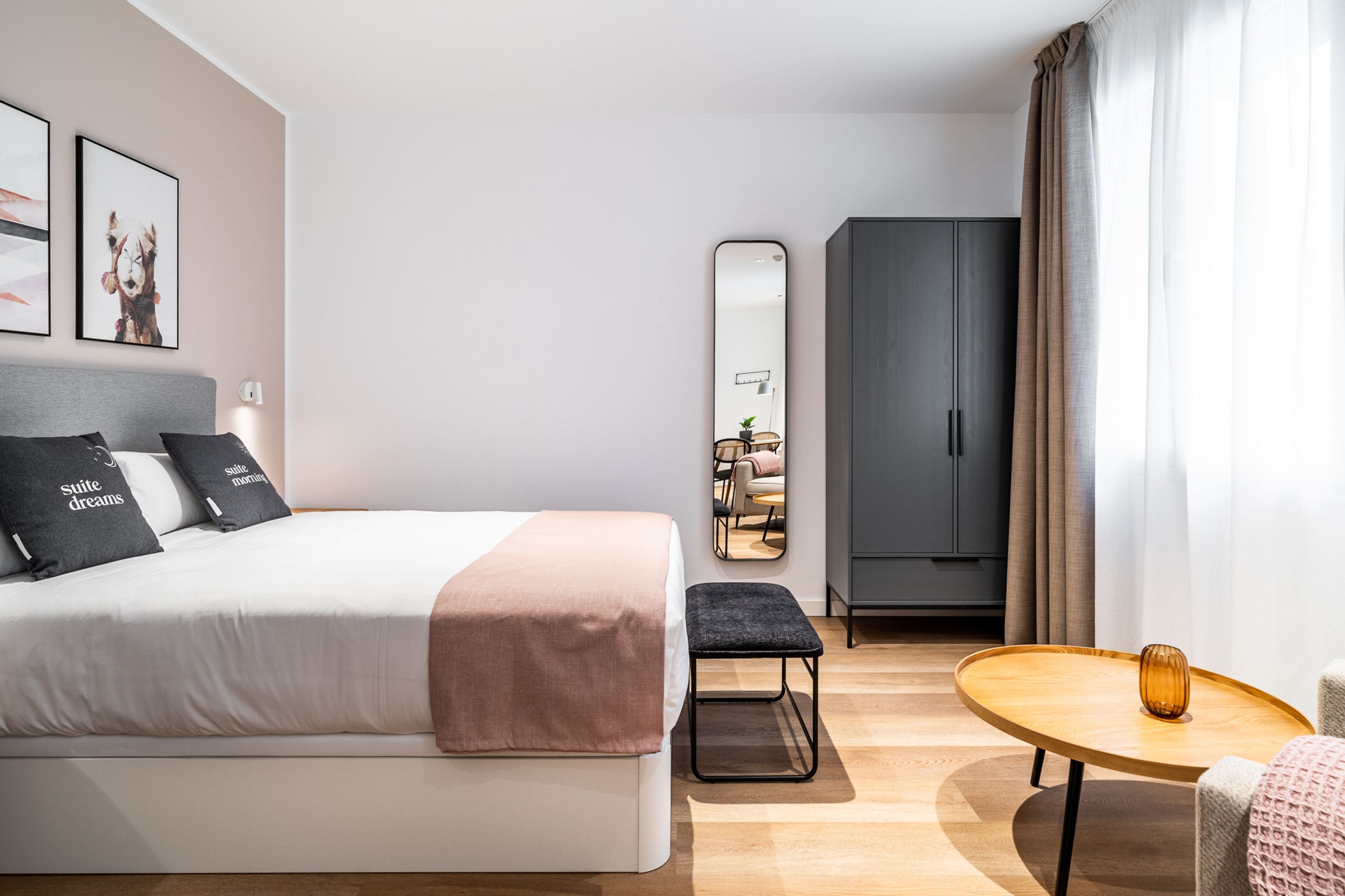 Una habitación de hotel moderna con una cama, una mesita, un banco, un armario y un espejo.