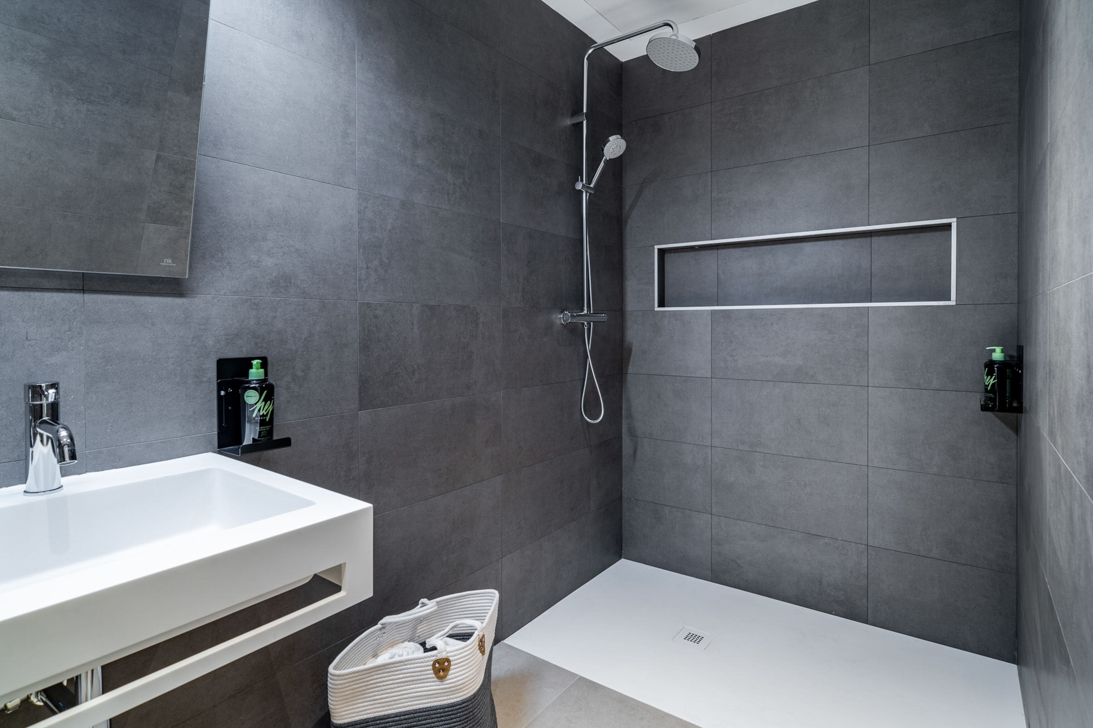 Un baño moderno con un lavamanos blanco, ducha y estante empotrado.