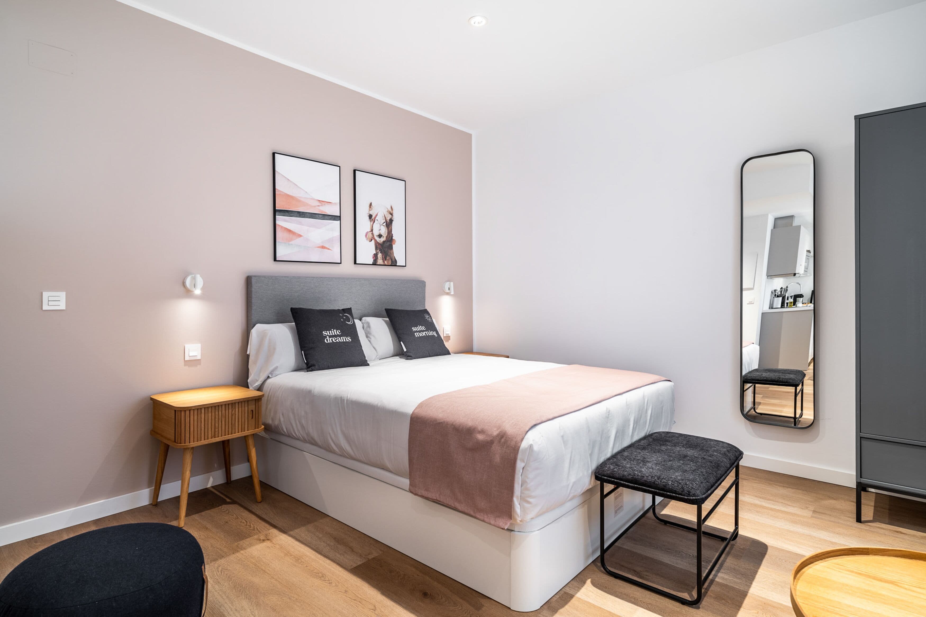 A modern bedroom with a bed, bedside tables, a bench, a mirror, and artwork on the wall.