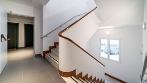 A modern interior with a curved staircase, a hallway leading to doors, and a window providing a view. - Limehome Sevilla Ronda de Capuchinos (Seville)