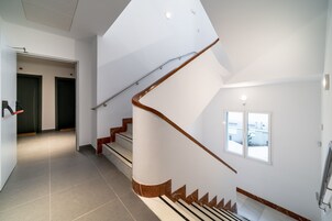 A modern interior with a curved staircase, a hallway leading to doors, and a window providing a view.