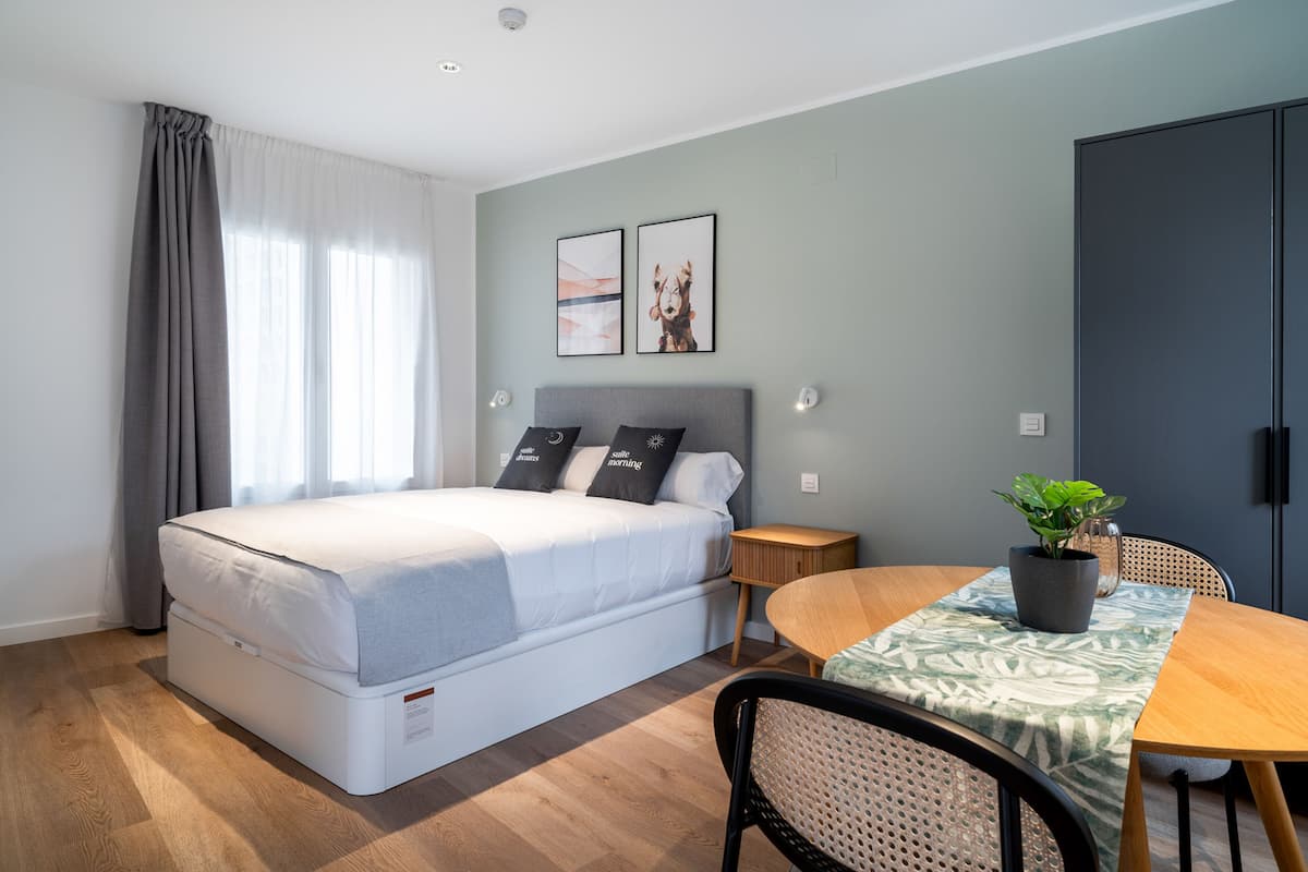 A modern bedroom with a bed, bedside table, and a small dining area with a table and chairs.