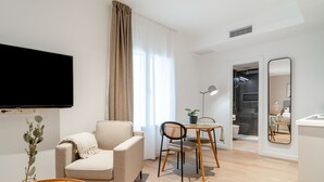 A modern living room with a sofa, a dining table with chairs, a TV mounted on the wall, and a large mirror. - Limehome Sevilla Ronda de Capuchinos (Seville)