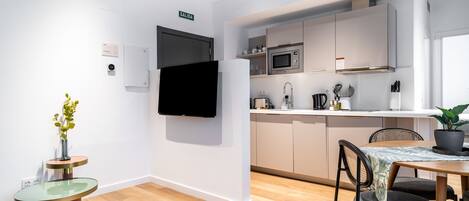 A modern kitchen with white cabinets, a microwave, and a sink. There is a dining table with chairs and a potted plant.