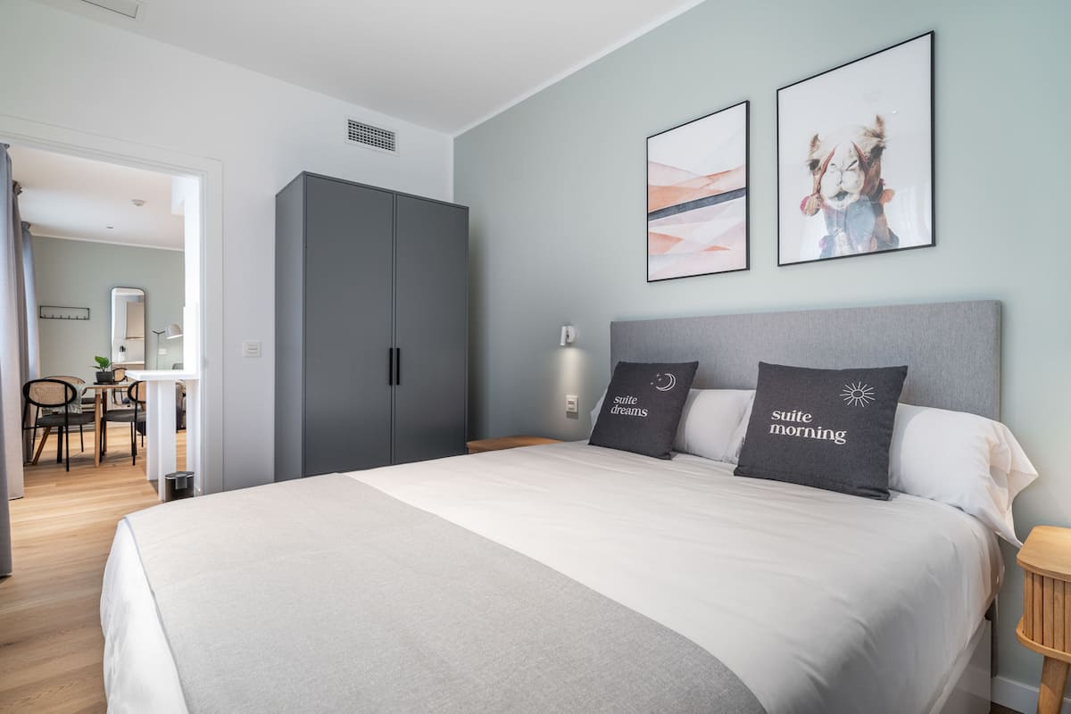 A bedroom with a large bed, two pillows with text, a grey wardrobe, and a desk with a chair.