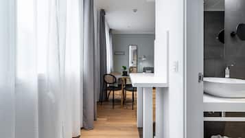 Una habitación de hotel moderna con piso de madera, un área de comedor con mesa y sillas, un lavamanos blanco y un espejo.
