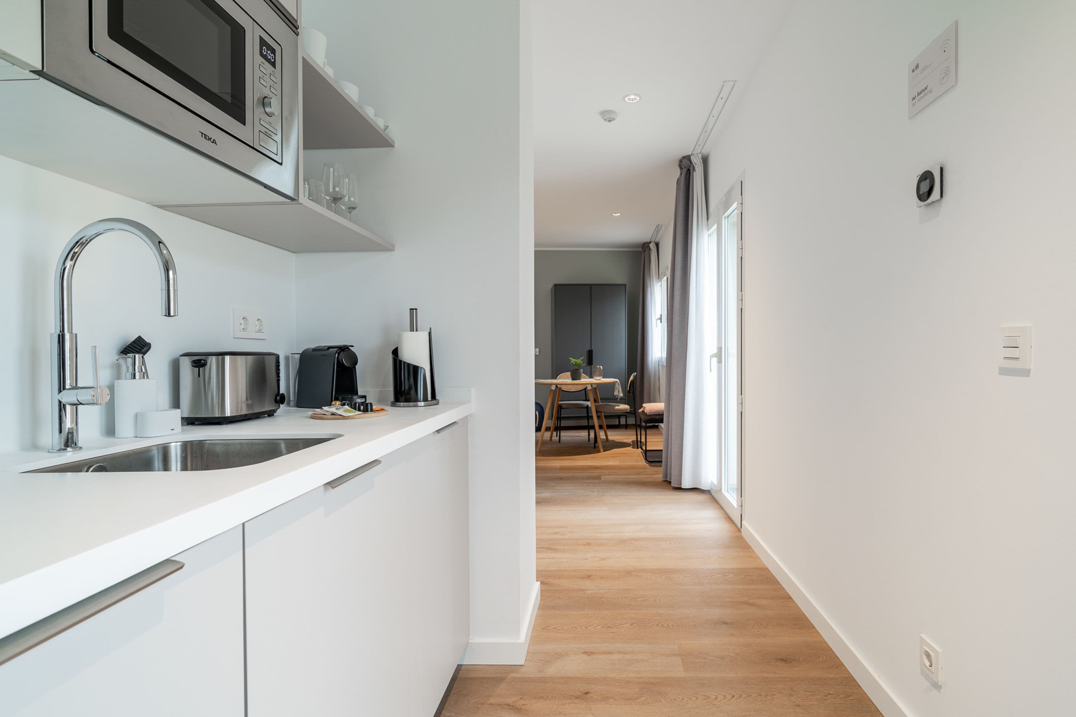 Una cucina moderna con microonde, tostapane e macchina del caffè. Si intravede sullo sfondo un'area pranzo con tavolo e sedie.