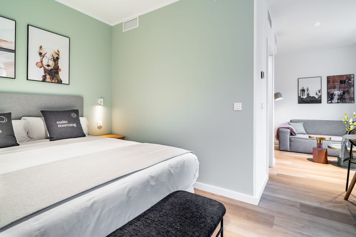 A modern hotel room with a large bed, a bench, a sofa, and a small table.