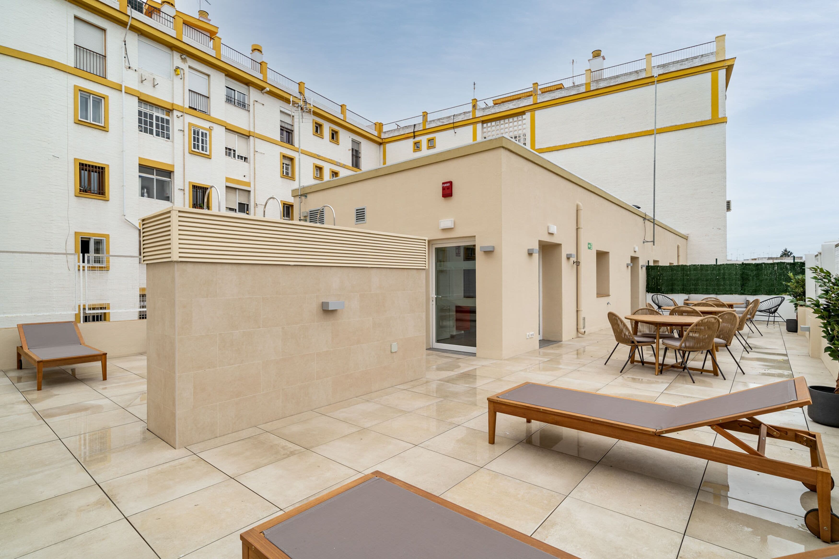 Un patio moderno al aire libre con una zona de estar, un edificio pequeño y vista de un edificio residencial al fondo.