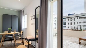 A modern room with a balcony, a dining area, and a view of buildings. - Limehome Sevilla Ronda de Capuchinos (Seville)