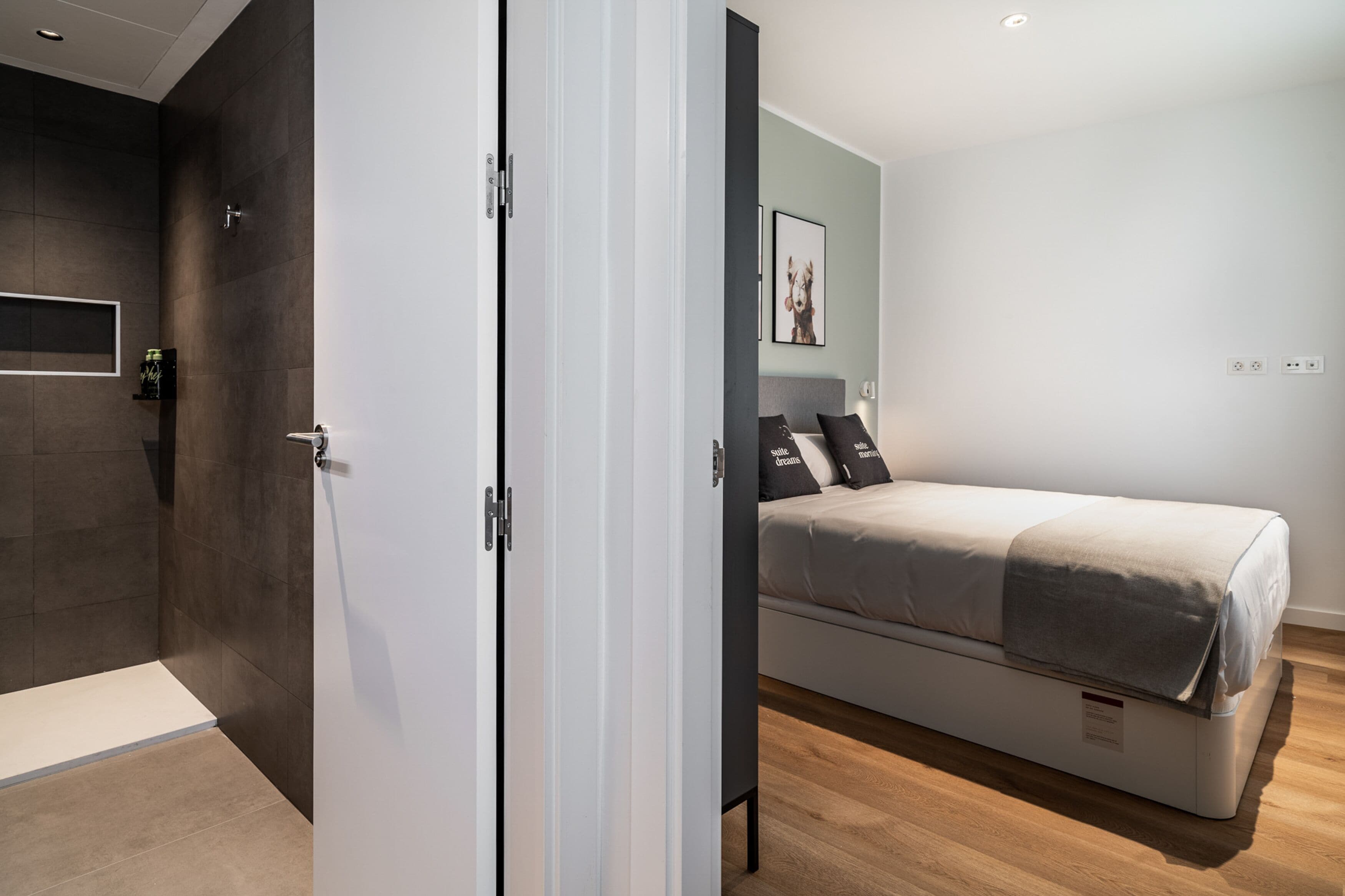 Un dormitorio moderno con una cama, una puerta y un estante pequeño con una botella.
